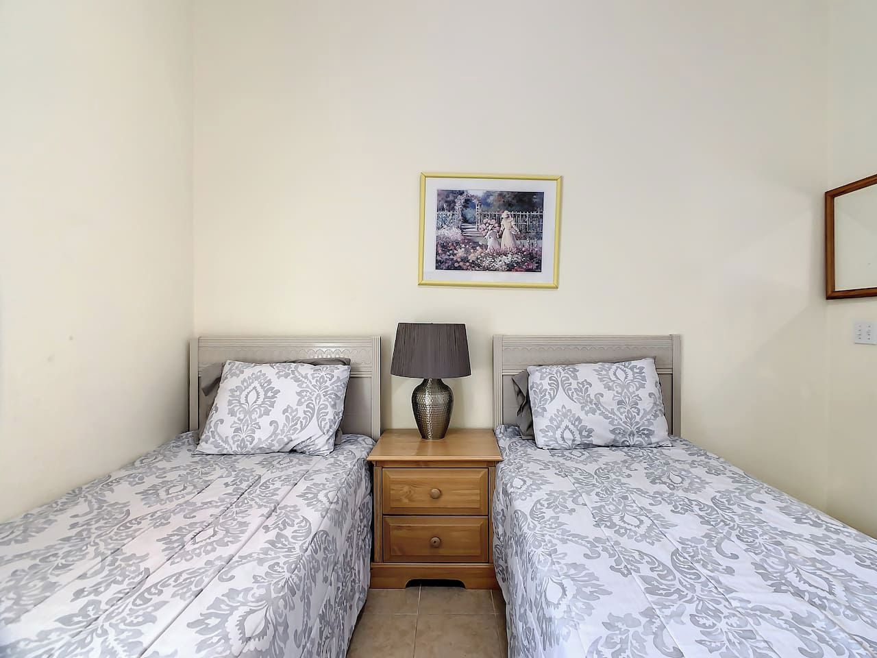 A twin room with two beds, a nightstand with a lamp, and a framed picture on the wall.