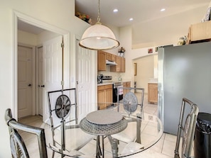 A modern kitchen with a dining area, including a glass table and chairs, a hanging light fixture, and wooden cabinets.
