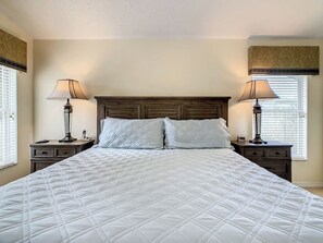 A neatly made bed with a quilted white comforter, flanked by two bedside tables with lamps, in a room with a wooden headboard and a window with blinds. - Conservation View, Hot Tub, Very Private (Kissimmee)