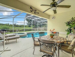 A covered outdoor area with a pool, lounge chairs, and a table with chairs.