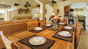 Comedor con una mesa de madera dispuesta para cuatro personas, rodeada de sillas, un jarrón con flores y una araña.