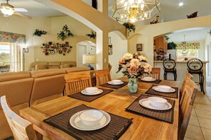 A dining area with a wooden table set for four, surrounded by chairs, a vase with flowers, and a chandelier. - Conservation View, Hot Tub, Very Private (Kissimmee)