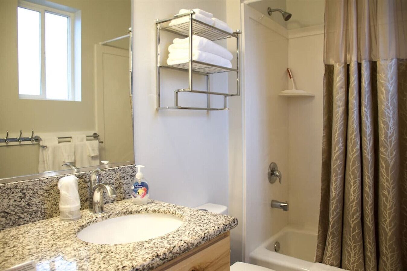 A bathroom with a granite countertop sink, a mirror, a towel rack, a shower with a glass door, and a toilet.