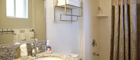 A bathroom with a granite countertop sink, a mirror, a towel rack, a shower with a glass door, and a toilet.