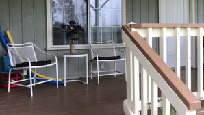 A covered porch with two white chairs, a small table, and a potted plant.