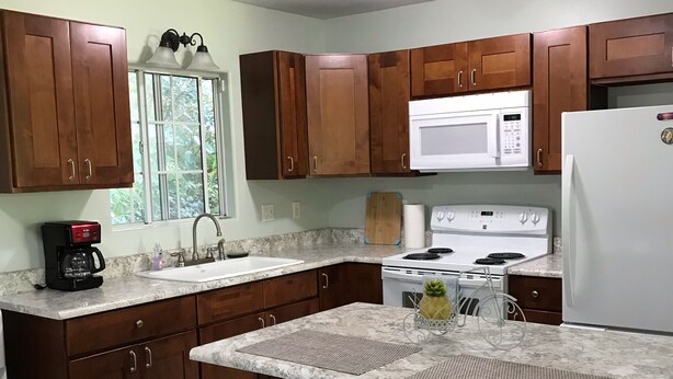 A kitchen with wooden cabinets, a microwave, a stove, and two wooden stools.