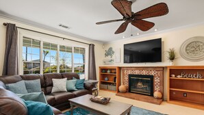 A living room with a leather sofa, a coffee table, a fireplace, and a ceiling fan.