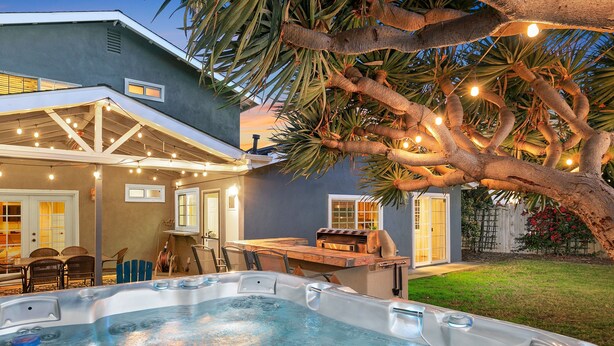 A backyard with a hot tub, outdoor seating, and string lights.