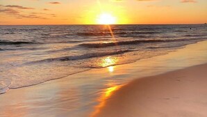 A beach scene with the sun setting over the ocean, reflecting on the water and sand.
