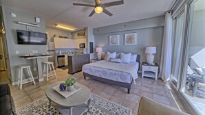 Habitación de hotel moderna con cama, escritorio, silla, televisor y zona de cocina.