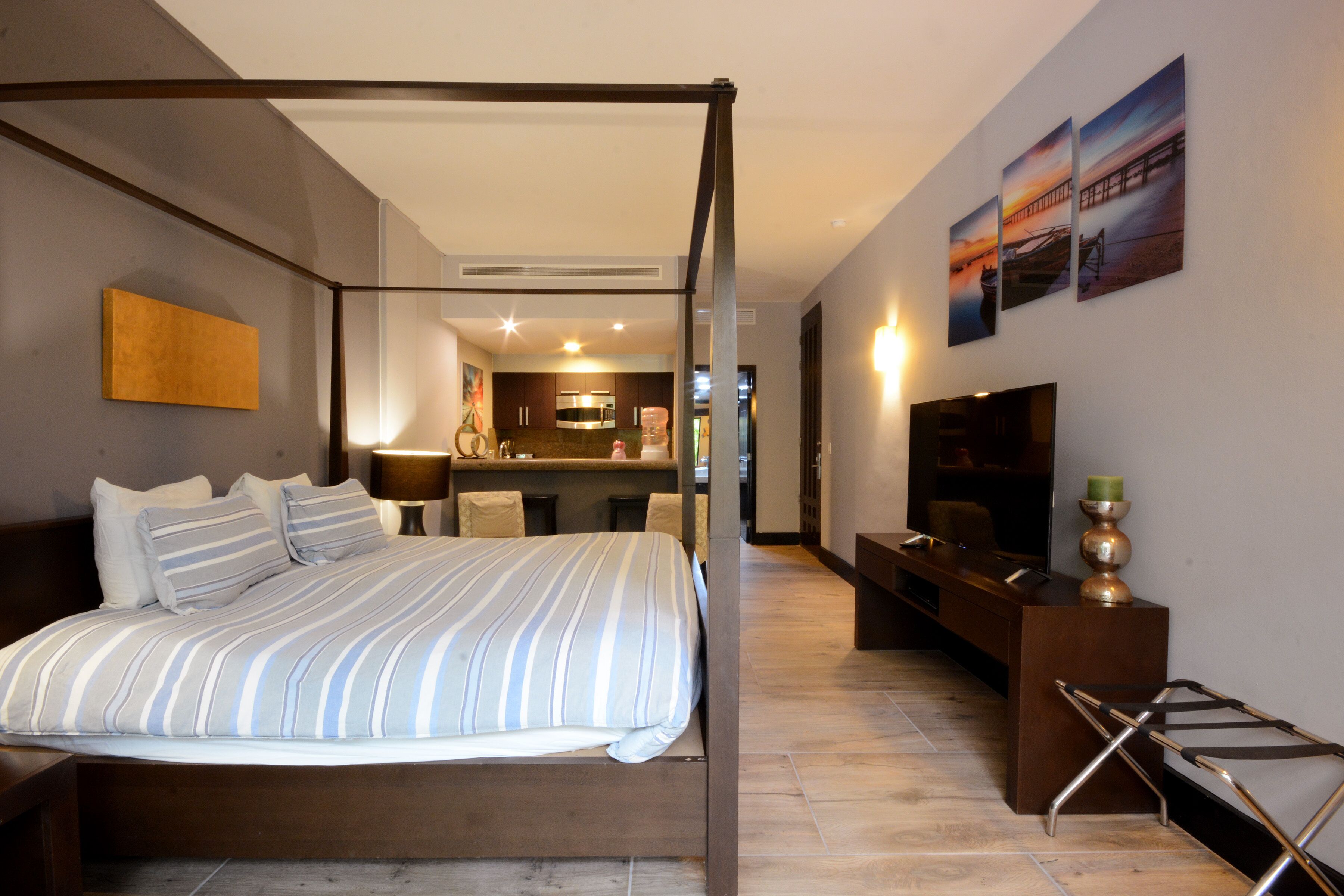 Un lit à baldaquin avec une couvre-lit à rayures, un téléviseur à écran plat, un bureau avec une chaise et une vue sur la cuisine et l’espace salon.