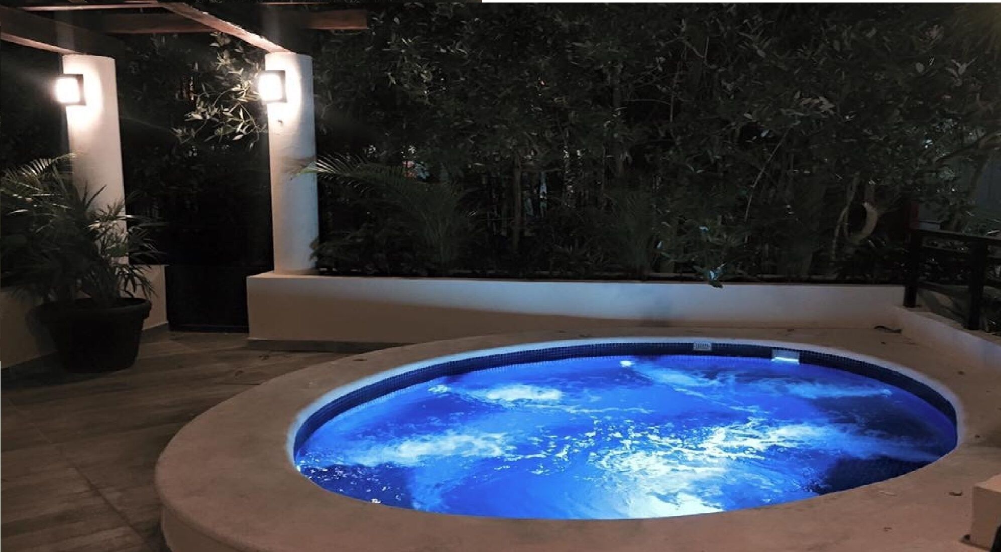 Un jacuzzi con interior azul, rodeado por una terraza de madera y plantas en macetas.