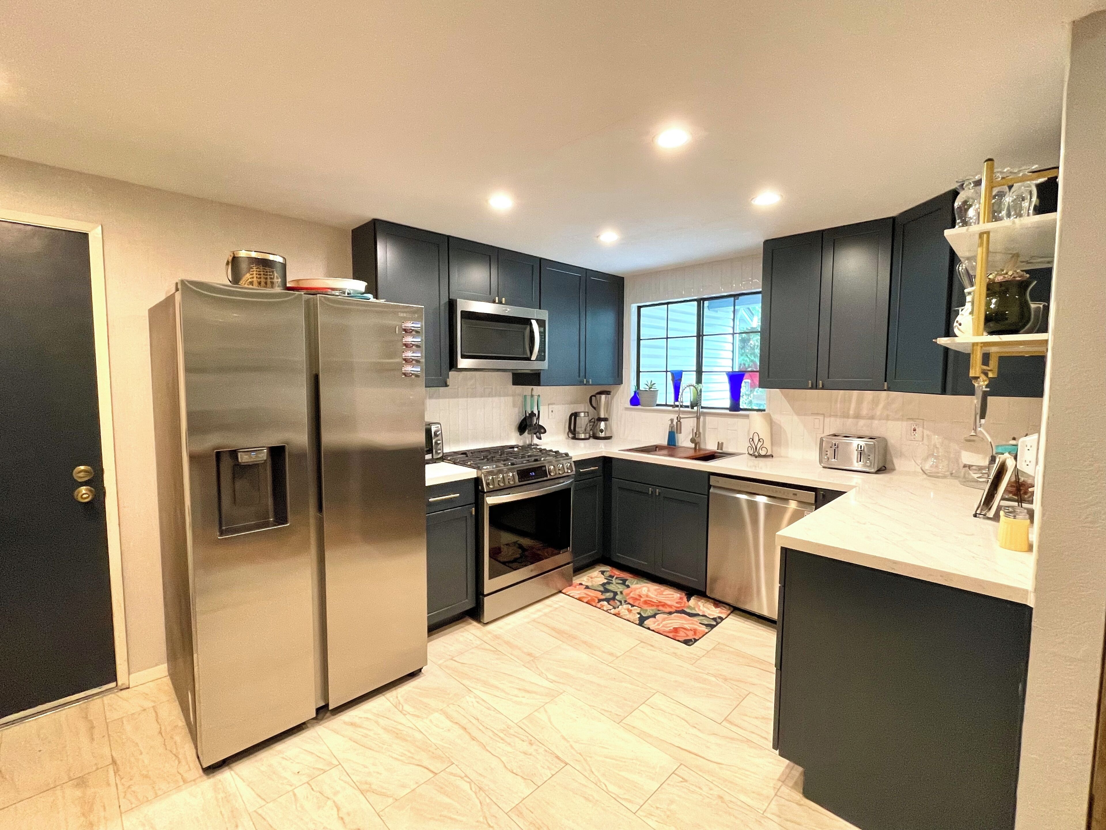 A modern kitchen with dark cabinets, stainless steel appliances, and a window providing natural light.