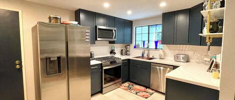 A modern kitchen with dark cabinets, stainless steel appliances, and a window providing natural light.