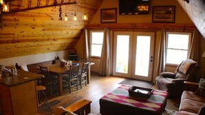 A cozy cabin interior with a wooden ceiling, a dining area, a sofa, and a large window. - Cozy A-Frame house in heart of the midwest!!! (Quincy)
