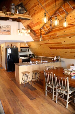 Una cocina acogedora con vigas de madera, una isla central, taburetes de bar y una mesa de comedor.