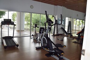 A gym with cardio machines, weight equipment, and large windows offering a view of the outdoors. - Sandy Beach Condo 17D (Cha-am)