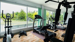 Un gimnasio con equipo de ejercicio diverso, amplias ventanas y vistas a zonas verdes.