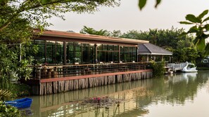 A riverside restaurant with outdoor seating, a dock, and a swan sculpture. - Rai Fahpratan Home and Garden (Hua Hin)