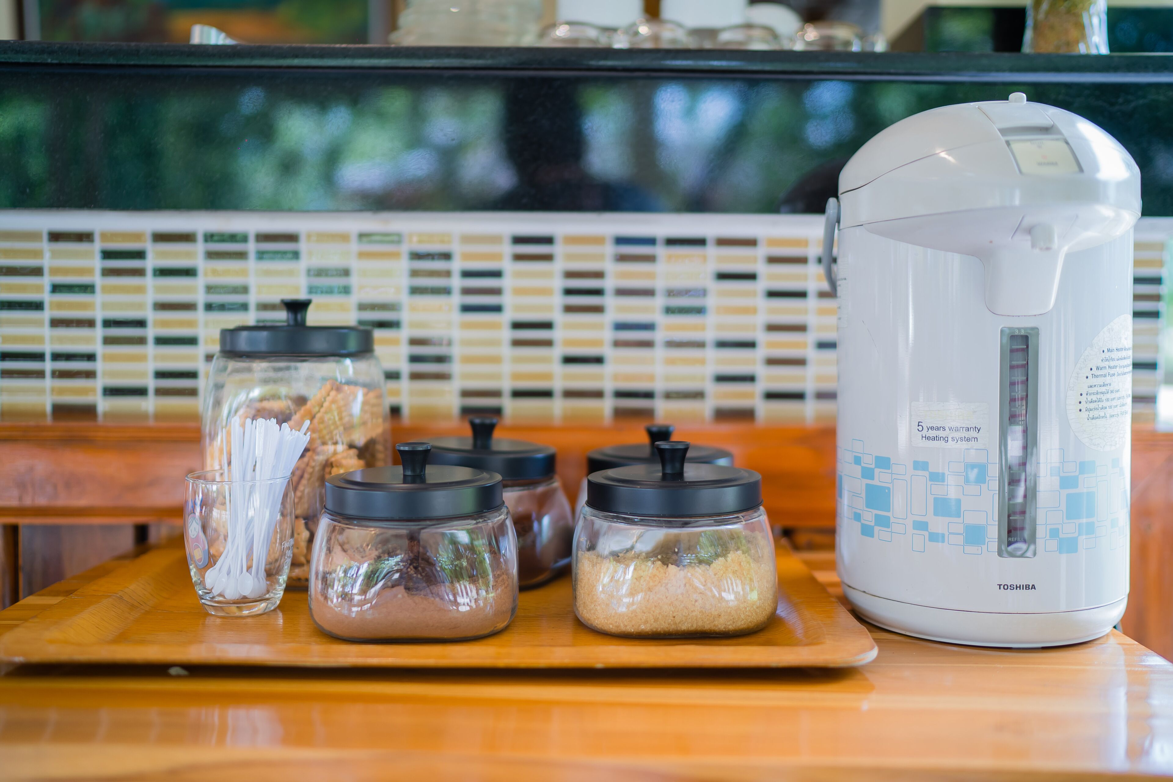 A kitchen counter with a white electric kettle, four glass containers with lids, and a tray.