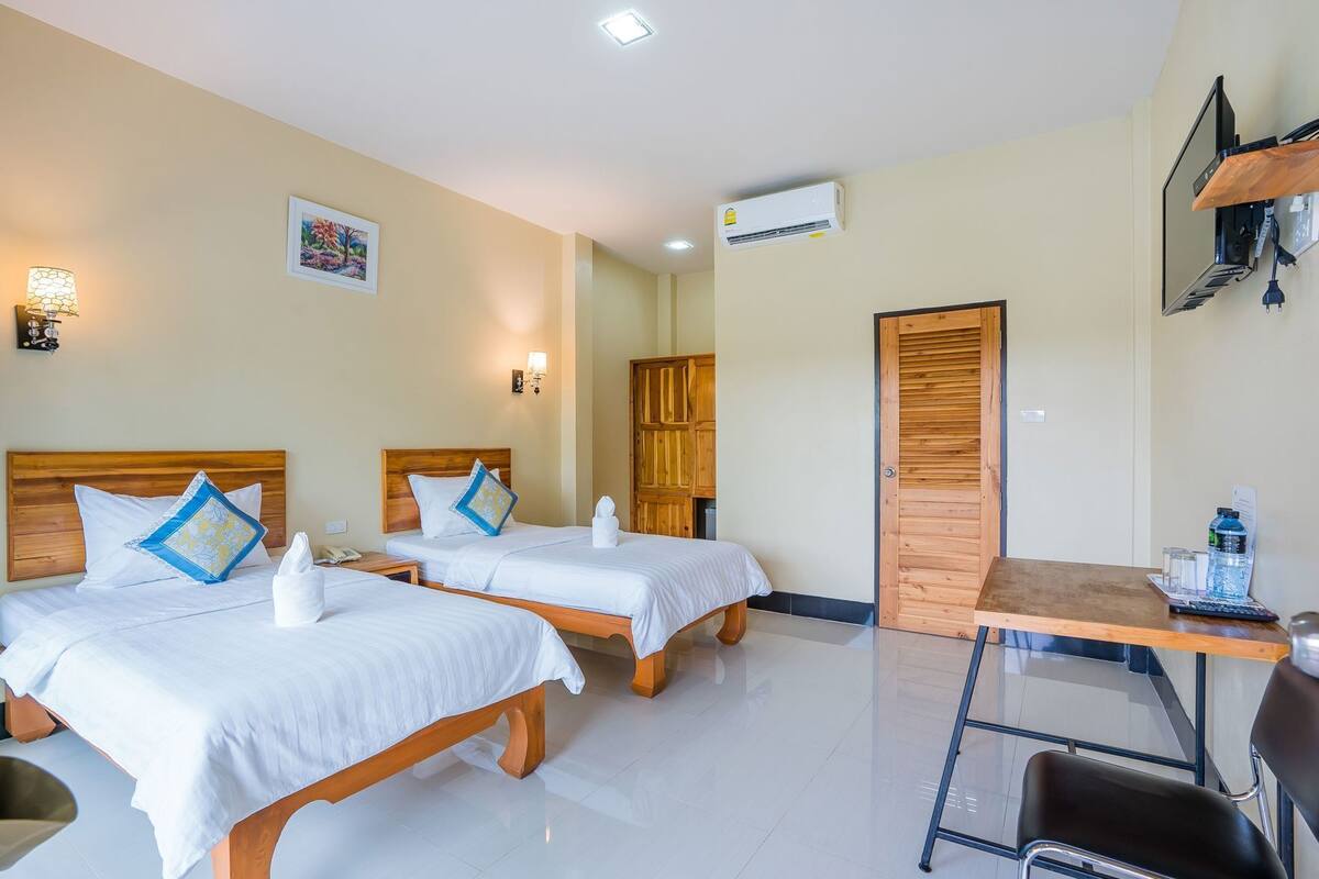 Habitación de hotel con dos camas, un escritorio, una silla, un aire acondicionado y un televisor montado en la pared.