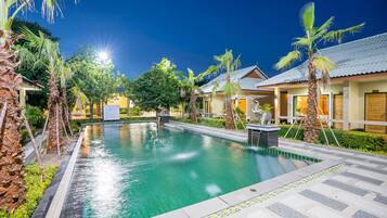 A swimming pool surrounded by palm trees and a building with a tiled roof.