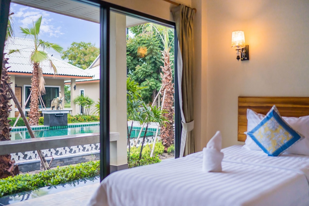 Habitación de hotel con cama, ventana con vista a una piscina y palmeras, y una luz nocturna en la pared.