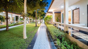 A pathway lined with trees and a tiled walkway leading to a building with a tiled roof and a wooden door.