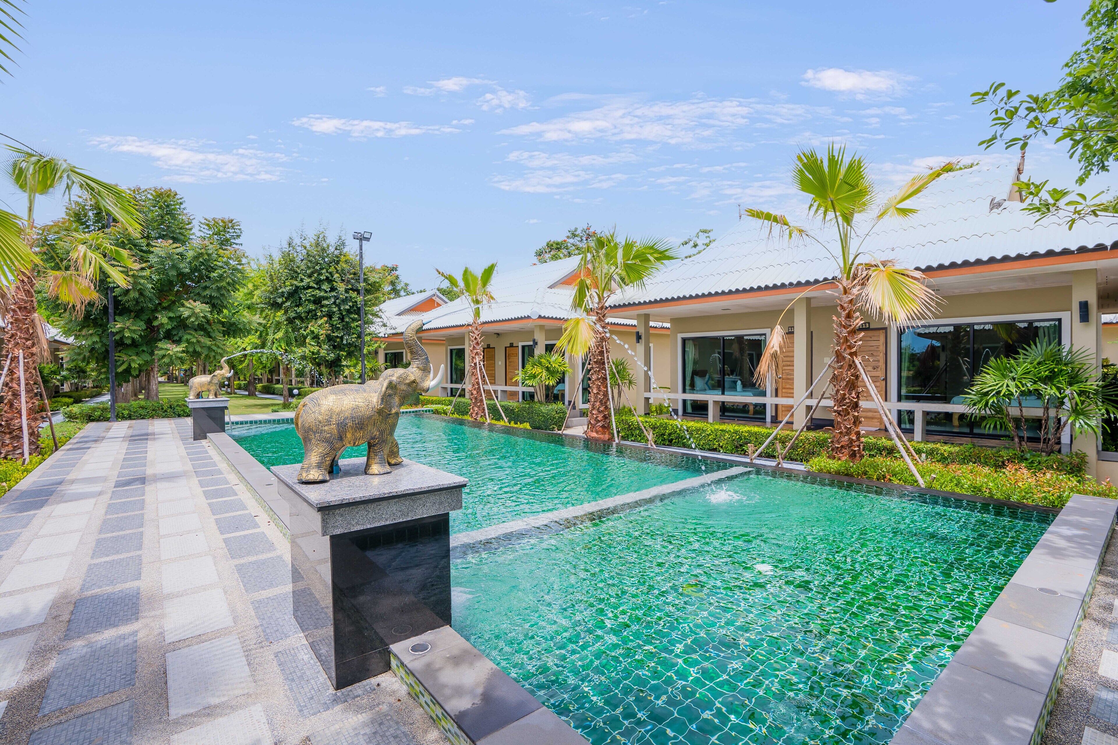 Una piscina con una estatua de elefante de piedra, rodeada de palmeras y edificios modernos.