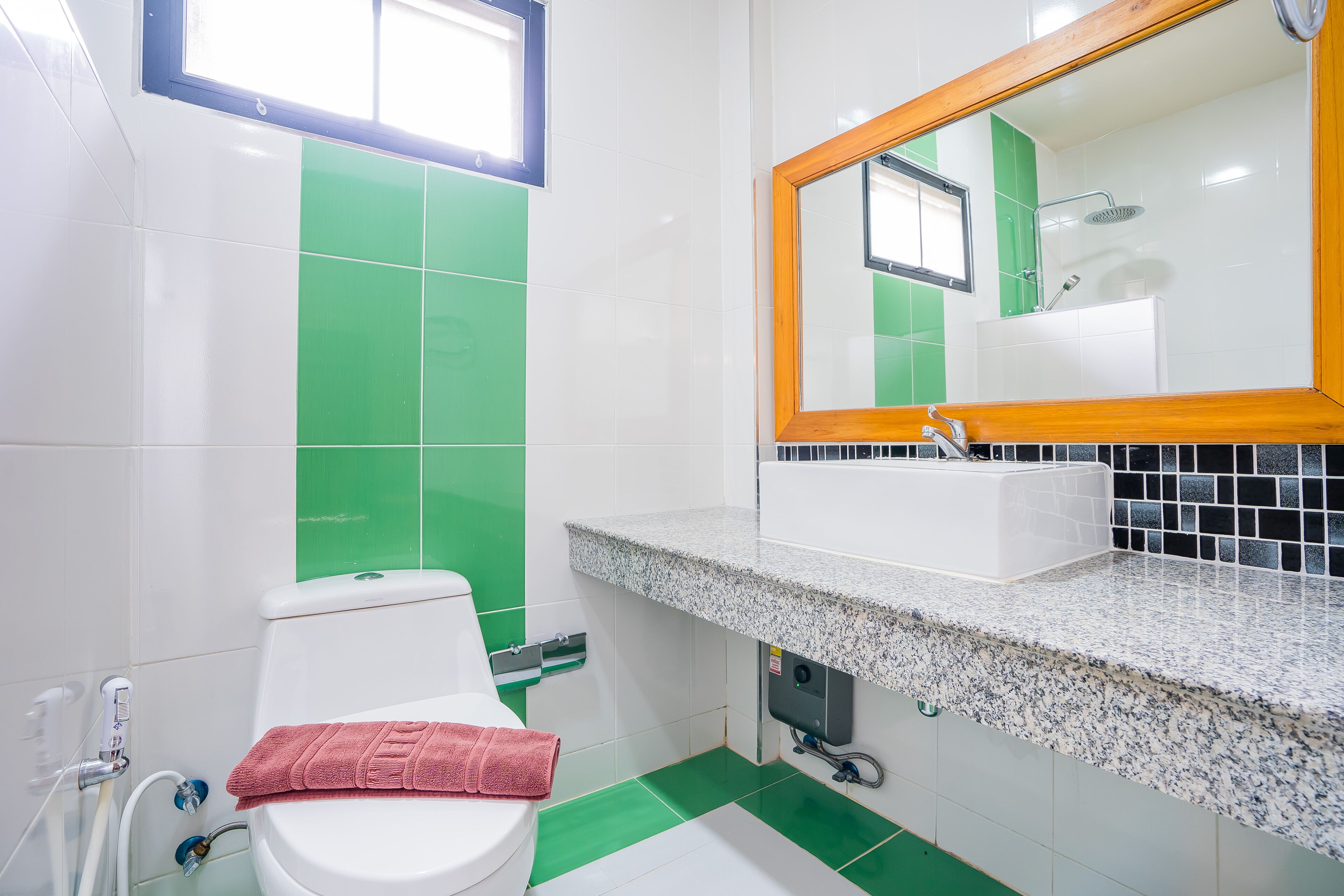 A bathroom with a white toilet, green and white tiles, a sink with a mirror, and a shower.