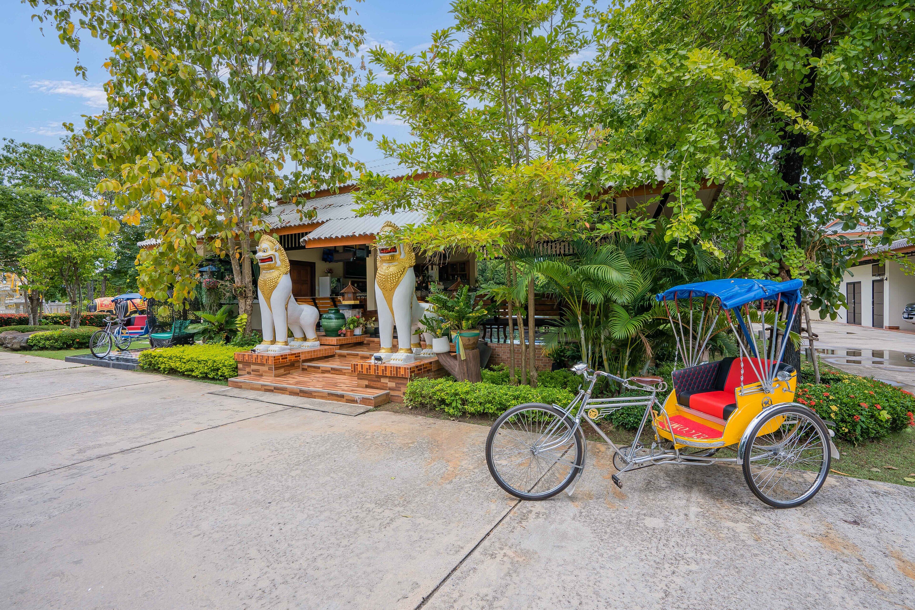A traditional rickshaw parked in front of a building with a statue and a staircase leading to the entrance.