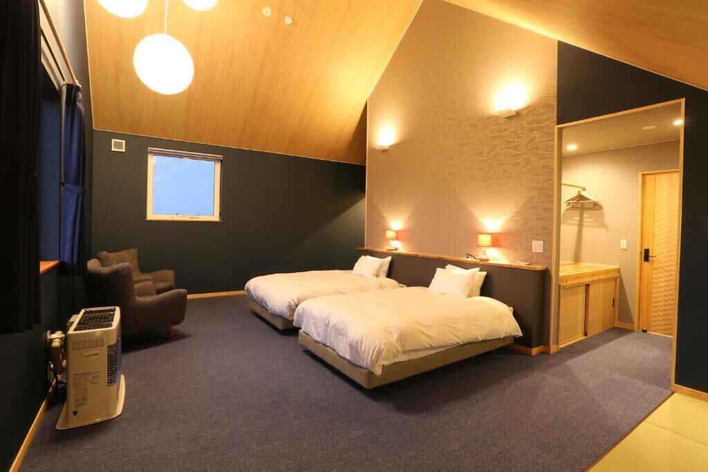 Une chambre avec un grand lit, un bureau et une chaise. Il y a une fenêtre et un radiateur au sol.