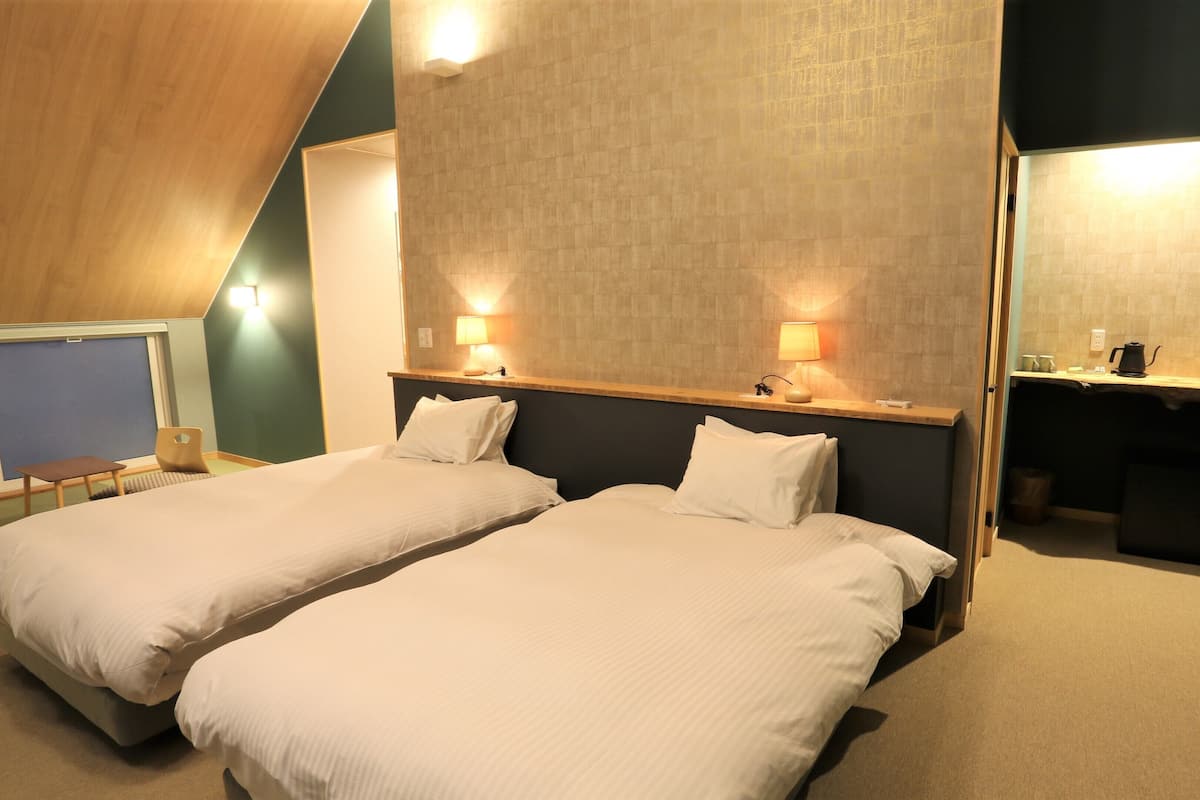 Una camera d'albergo con due letti, una scrivania con sedia e un angolo cottura.