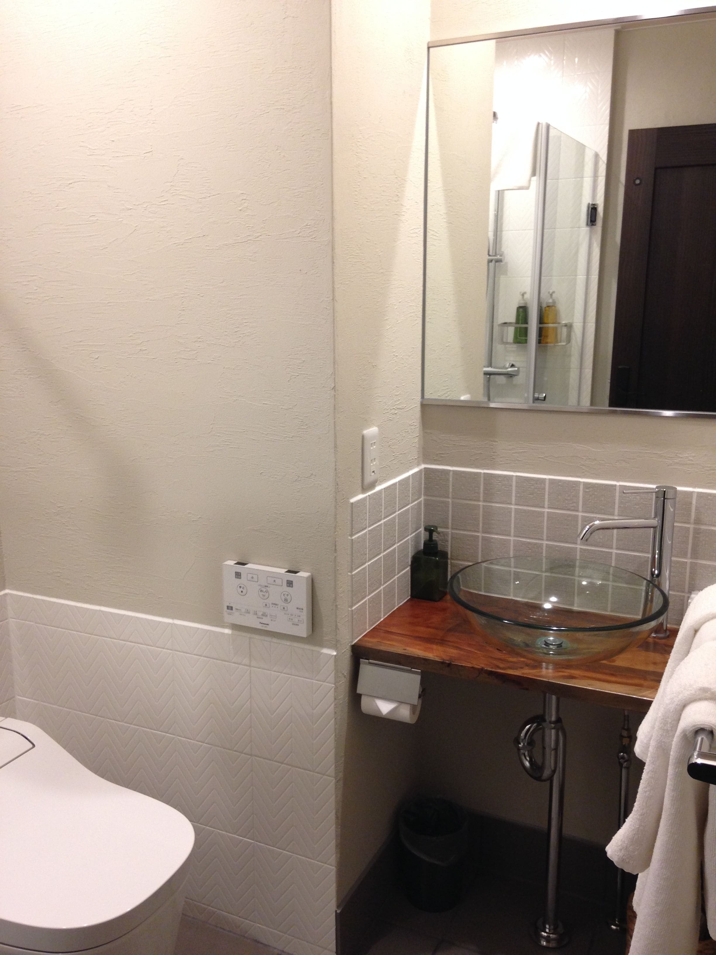 Un baño con lavamanos de vidrio, encimera de madera, toallero, espejo y retrete.
