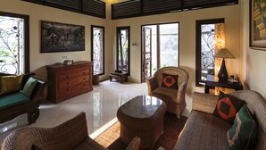 A spacious living room with wicker furniture, a wooden cabinet, and a large painting on the wall. - Murni's Villa Kelor (Ubud)