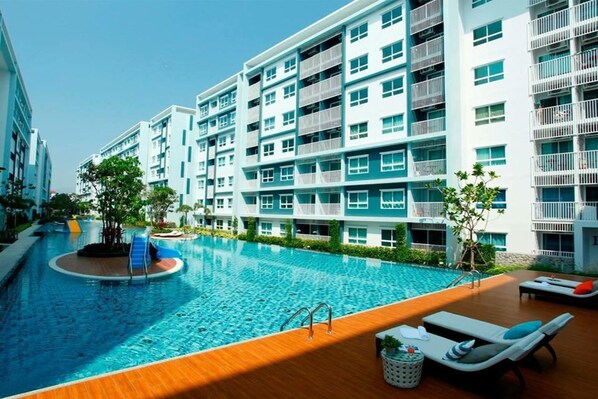 Un hotel moderno con piscina, varios balcones y una zona de terraza de madera.