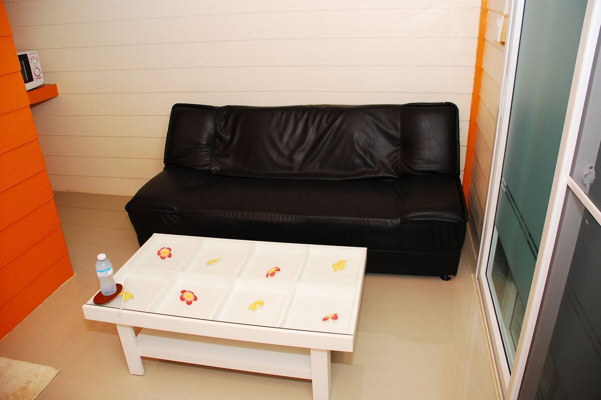 Een kleine kamer met een zwarte leren bank, een witte bijzettafel met bloemmotieven en een waterfles op de tafel.