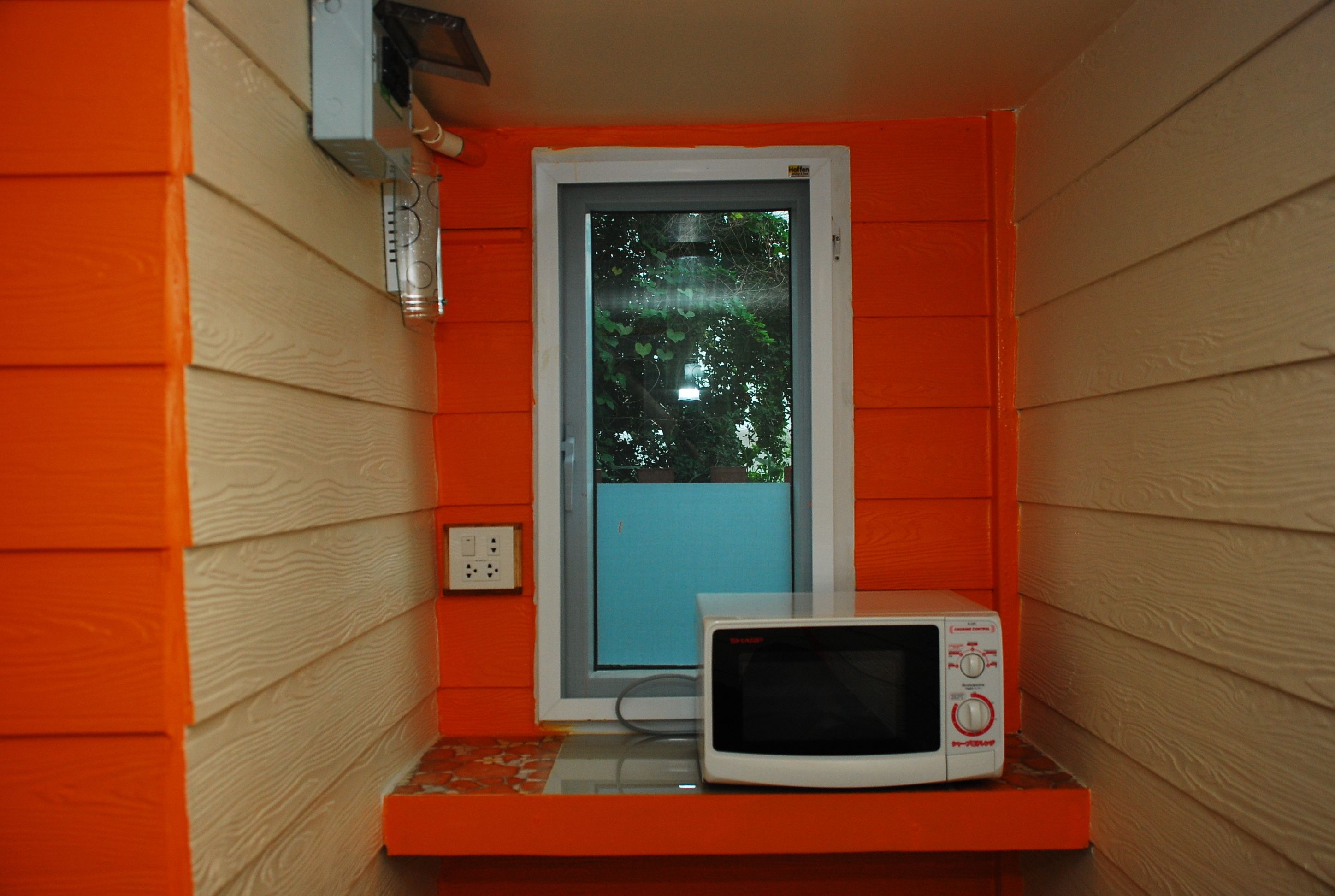A small room with orange walls, a window, and a microwave on a shelf.