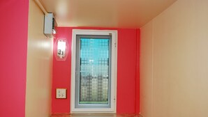 A bathroom with a red wall, a window with a metal grid, and a light switch on the wall. - Baan Kum Siri (Hua Hin)