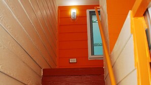 A staircase with red steps and a yellow handrail, leading to an orange wall with a door and a light fixture. - Baan Kum Siri (Hua Hin)