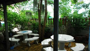 A covered outdoor seating area with multiple tables and benches, surrounded by trees and a brick floor. - Baan Kum Siri (Hua Hin)