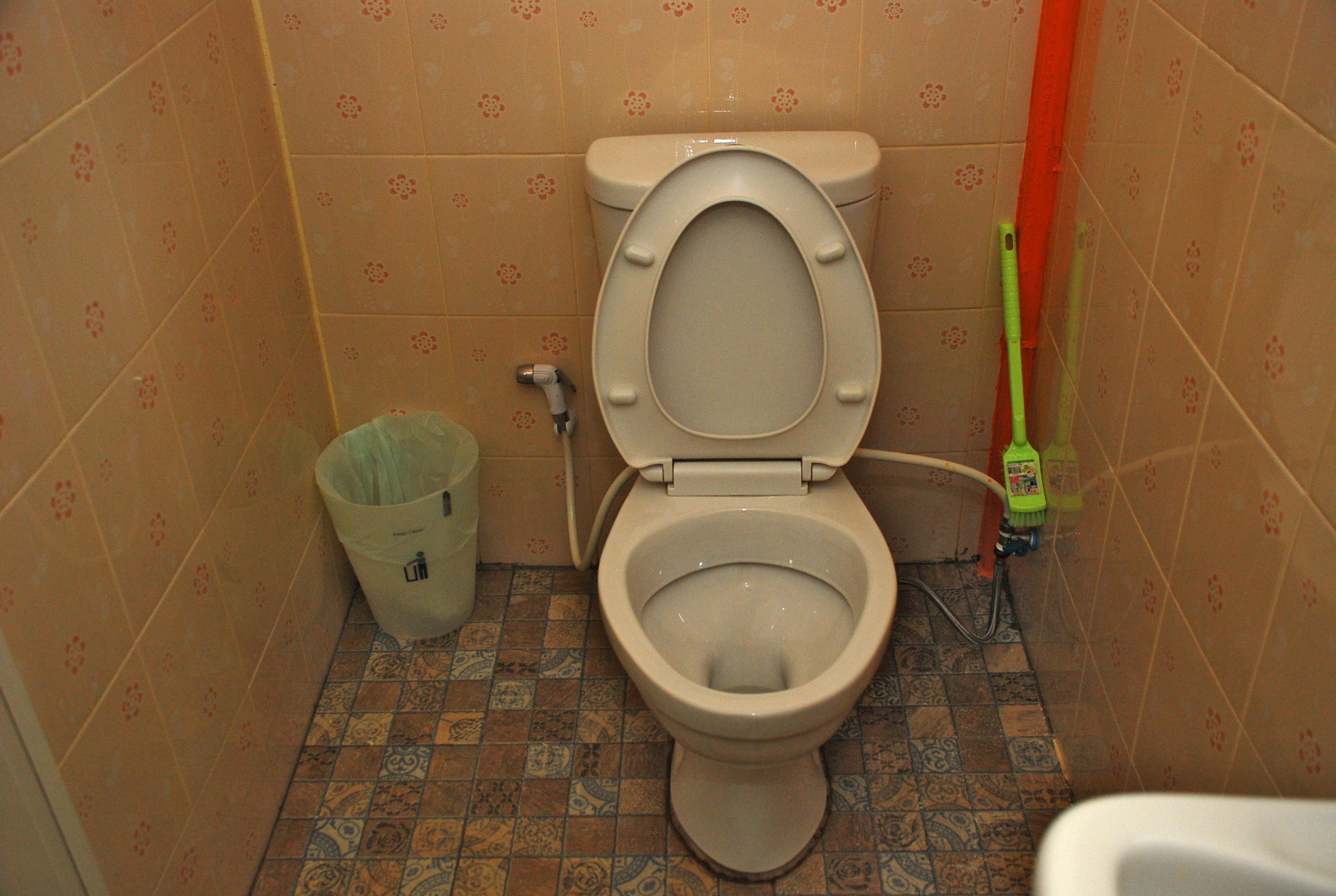 A small bathroom with a toilet, a trash can, and a cleaning brush.