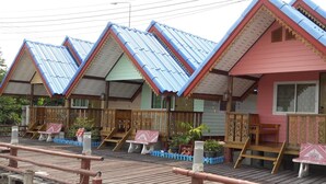 Uma fileira de cabanas de madeira com telhados azuis e paredes cor-de-rosa, com grades e bancos de madeira.