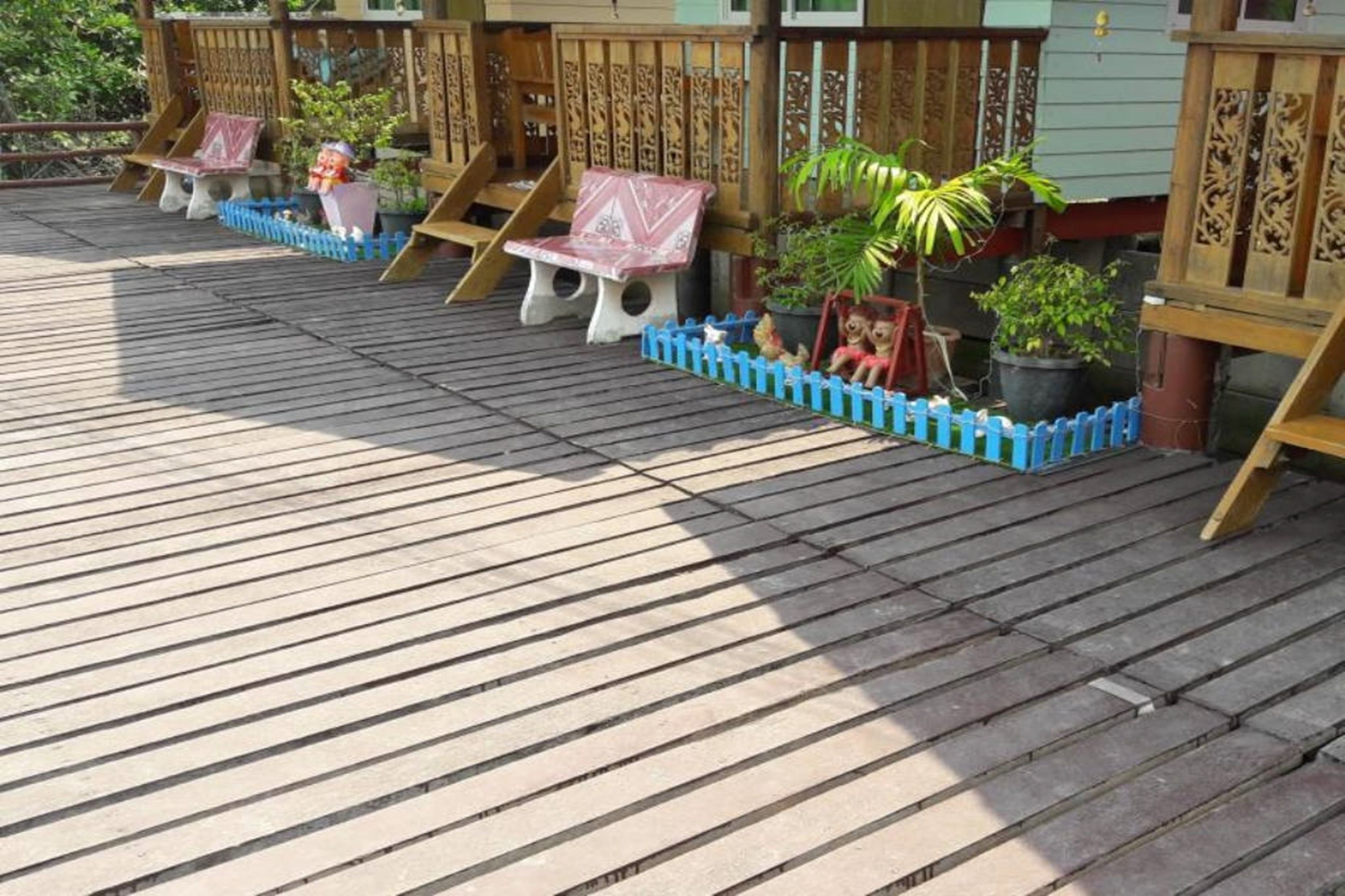 A wooden deck with a blue fence, wooden chairs, and potted plants.