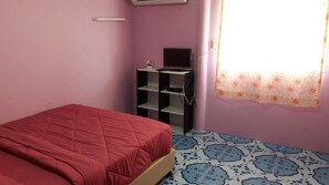 Un dormitorio con una cama, un televisor en una estantería y suelo estampado.