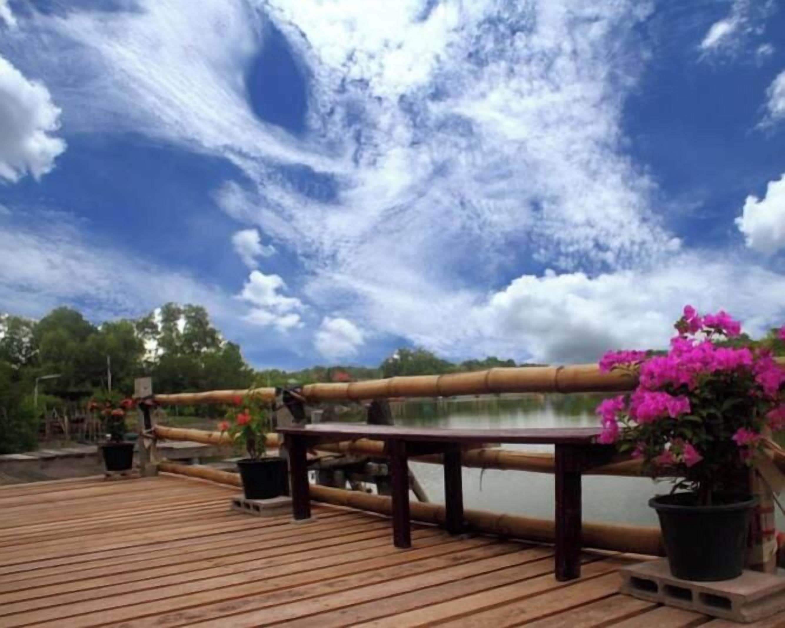 Un terrazza in legno con ringhiera che si affaccia su uno specchio d'acqua, circondata da vasi con piante e fiori.