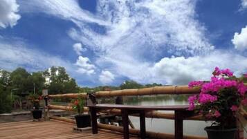 A wooden deck with a railing overlooking a body of water, surrounded by potted plants and flowers.