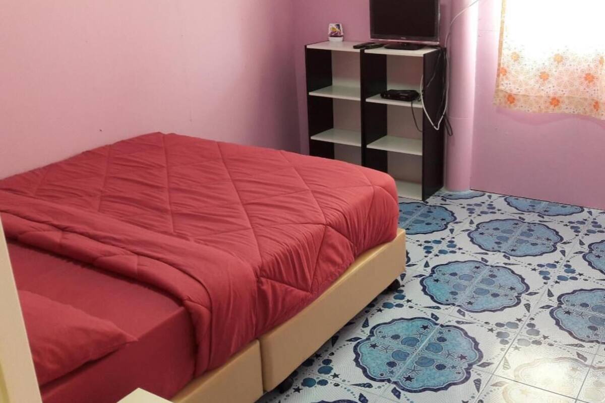 Une chambre à coucher avec un lit, un téléviseur posé sur une étagère et des carreaux de sol à motifs.
