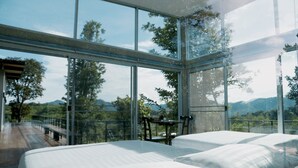 Une chambre moderne avec de grandes fenêtres, deux lits et une vue sur l’extérieur.