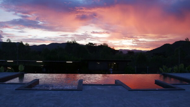 Une piscine avec vue sur le coucher de soleil, entourée d’un espace paysager et avec un bâtiment en arrière-plan.
